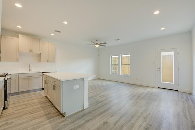 kitchen with stainless steel gas stove, white cabinetry, light hardwood / wood-style flooring, and a center island