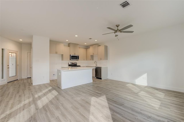 kitchen with appliances with stainless steel finishes, a kitchen island, sink, ceiling fan, and light hardwood / wood-style flooring