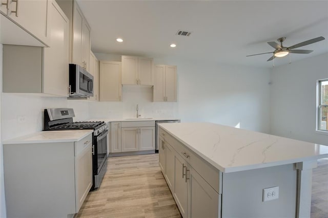 kitchen featuring light stone countertops, appliances with stainless steel finishes, a center island, sink, and light hardwood / wood-style flooring