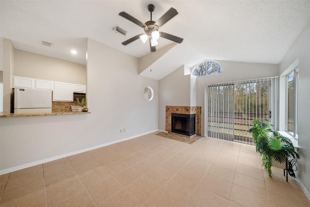 unfurnished living room with lofted ceiling, ceiling fan, a fireplace, a textured ceiling, and light tile patterned floors