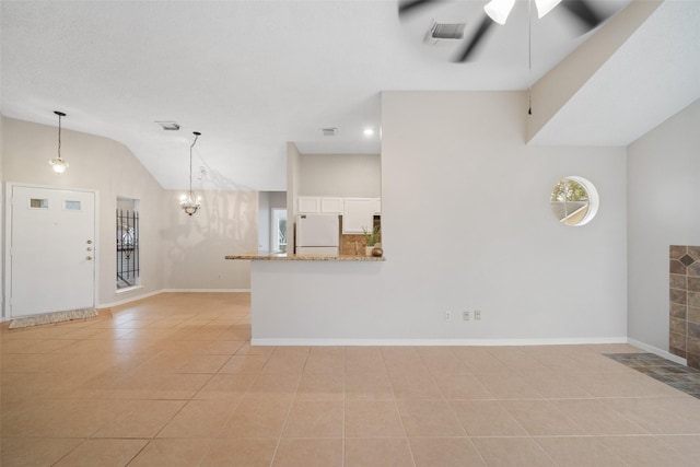 unfurnished living room with ceiling fan with notable chandelier, light tile patterned floors, and vaulted ceiling