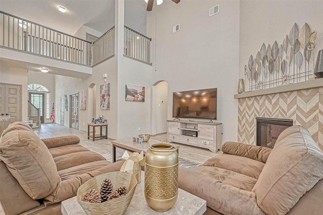 living room with ceiling fan, a tile fireplace, and a high ceiling