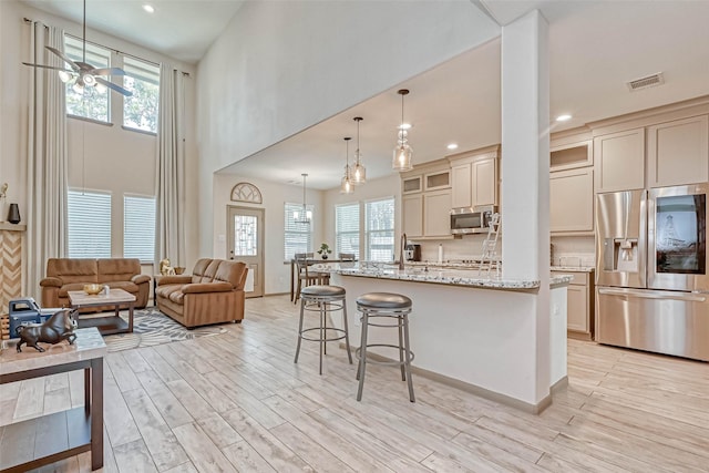 kitchen with stainless steel appliances, light hardwood / wood-style floors, hanging light fixtures, cream cabinets, and light stone counters