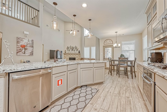 kitchen with appliances with stainless steel finishes, decorative light fixtures, light stone countertops, light hardwood / wood-style flooring, and sink