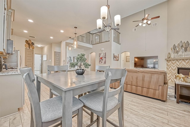 dining room with light hardwood / wood-style floors, a towering ceiling, and ceiling fan with notable chandelier