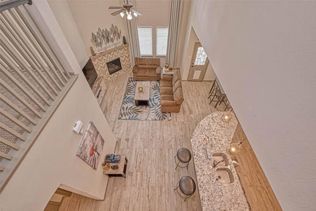 living room featuring ceiling fan, wood-type flooring, a towering ceiling, and a stone fireplace