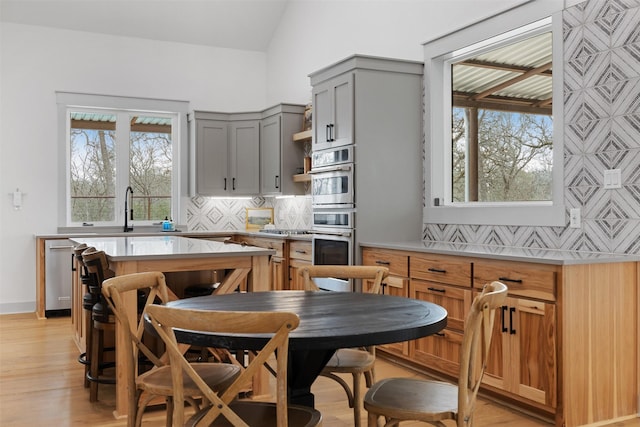 kitchen with gray cabinets, tasteful backsplash, light wood-type flooring, lofted ceiling, and sink