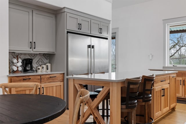 kitchen with backsplash, light hardwood / wood-style floors, high quality fridge, gray cabinetry, and a breakfast bar area