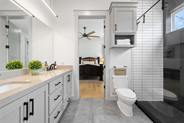 bathroom with toilet, vanity, ceiling fan, tile patterned flooring, and tiled shower