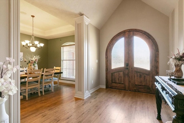 foyer with french doors, an inviting chandelier, ornate columns, and wood-type flooring