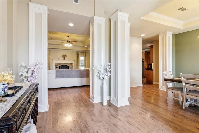 interior space featuring light wood-type flooring, ornate columns, ornamental molding, and a raised ceiling