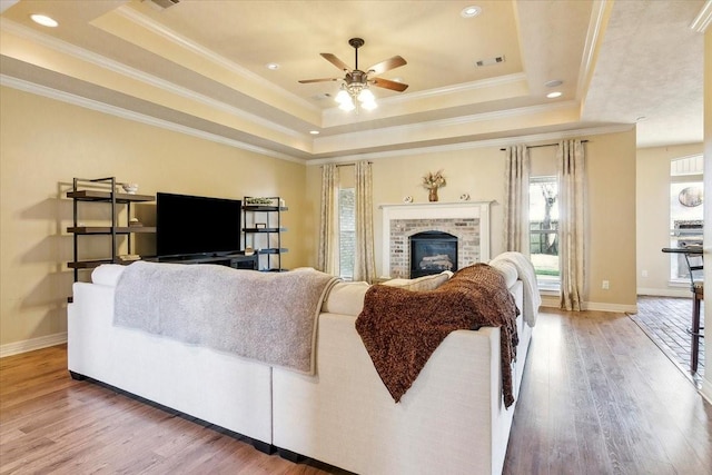 living room with crown molding, wood-type flooring, a brick fireplace, and a tray ceiling