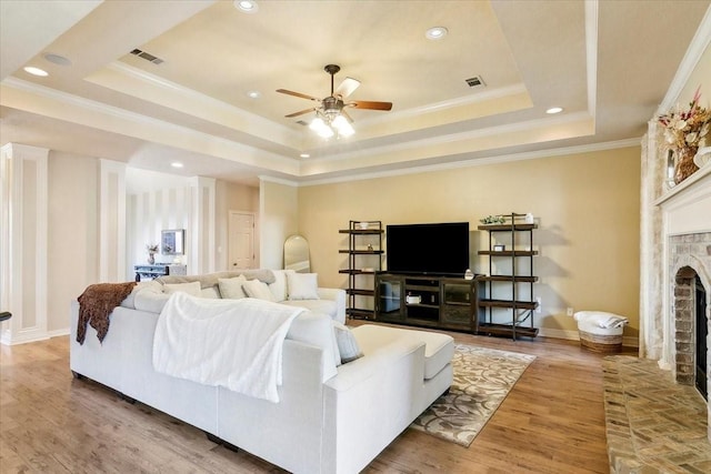 living room featuring hardwood / wood-style floors, a tray ceiling, ornamental molding, and a fireplace