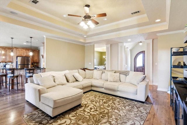 living room featuring a raised ceiling, wood-type flooring, ornamental molding, and ceiling fan