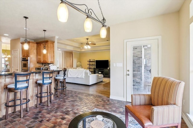 kitchen with ceiling fan, a raised ceiling, a kitchen bar, hanging light fixtures, and stainless steel oven