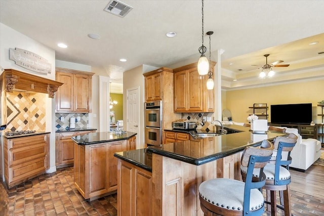 kitchen featuring kitchen peninsula, stainless steel double oven, decorative backsplash, decorative light fixtures, and sink