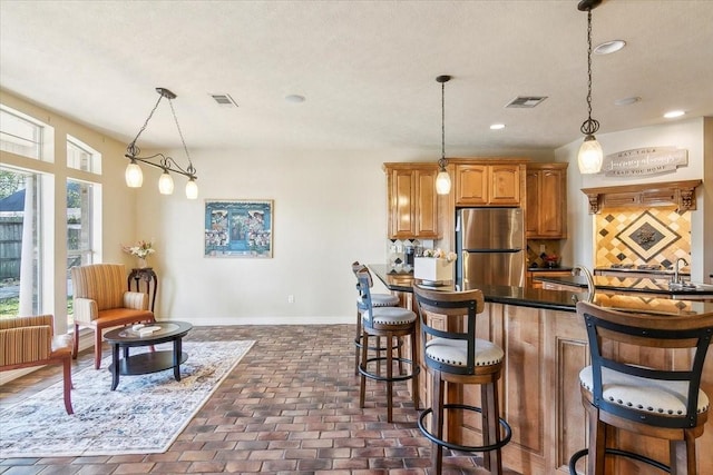 kitchen featuring radiator, decorative light fixtures, decorative backsplash, a kitchen breakfast bar, and stainless steel refrigerator