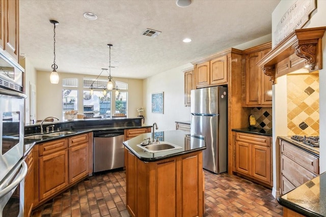 kitchen with appliances with stainless steel finishes, decorative light fixtures, tasteful backsplash, sink, and a kitchen island with sink