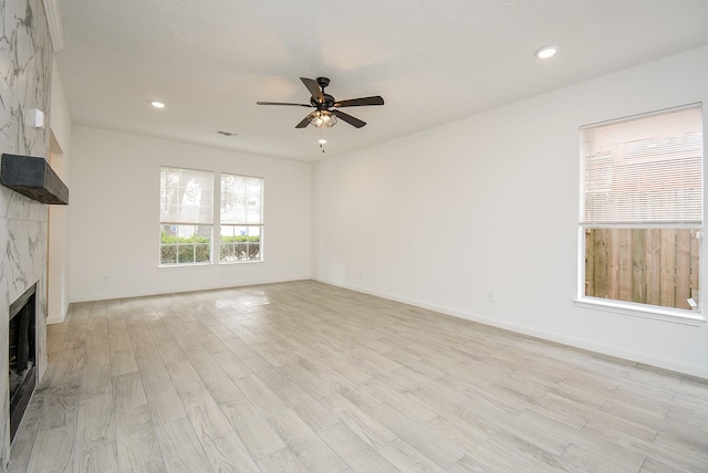 unfurnished living room featuring light wood-type flooring, ceiling fan, and a tiled fireplace