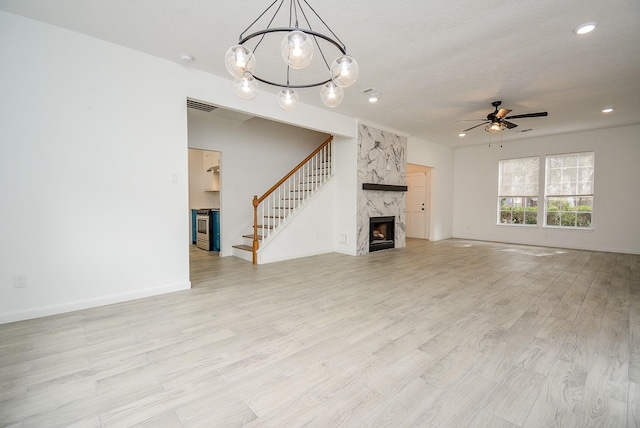 unfurnished living room featuring ceiling fan with notable chandelier, light wood-type flooring, and a fireplace