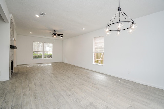 unfurnished living room featuring ceiling fan with notable chandelier, a large fireplace, light hardwood / wood-style flooring, and a textured ceiling