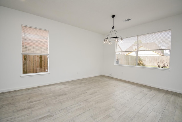 spare room featuring a chandelier and light wood-type flooring