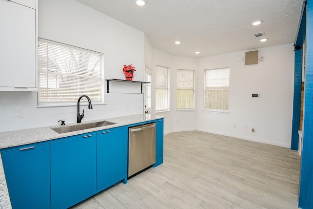 kitchen featuring light wood-type flooring, light stone countertops, a textured ceiling, stainless steel dishwasher, and sink