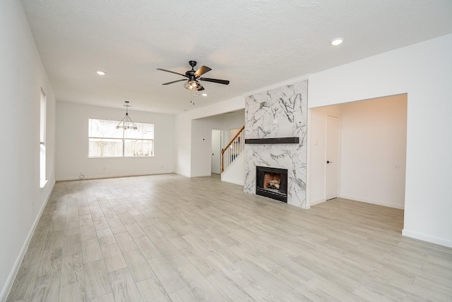 unfurnished living room featuring ceiling fan, light wood-type flooring, a premium fireplace, and a textured ceiling