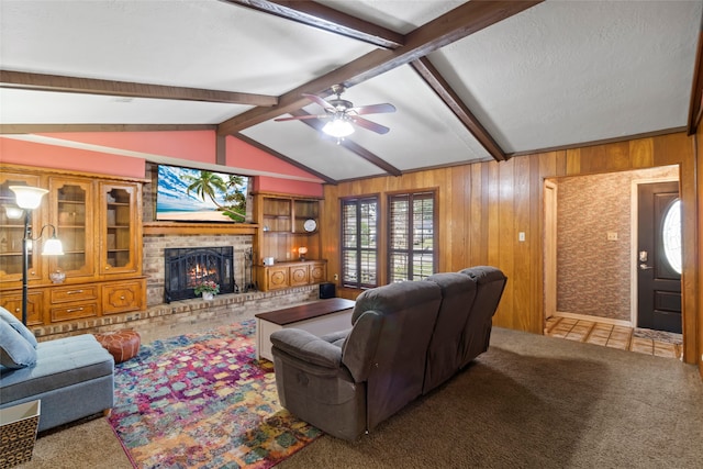 carpeted living room with a textured ceiling, vaulted ceiling with beams, ceiling fan, wood walls, and a brick fireplace