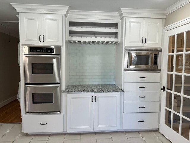 kitchen with light tile patterned floors, appliances with stainless steel finishes, white cabinetry, and light stone countertops