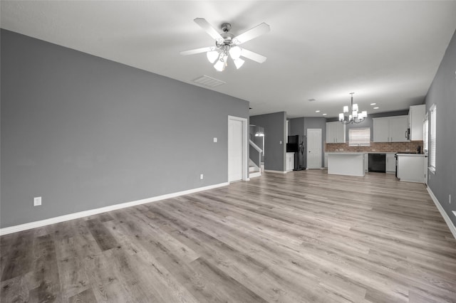 unfurnished living room with ceiling fan with notable chandelier and light hardwood / wood-style flooring