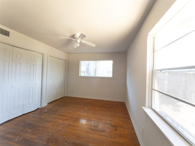 unfurnished bedroom with ceiling fan, dark wood-type flooring, and multiple closets