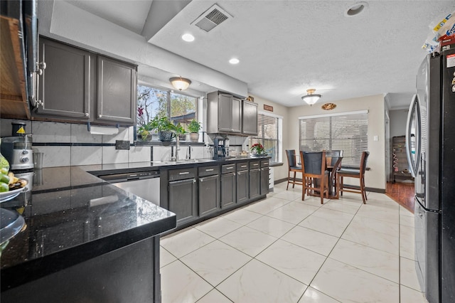 kitchen featuring sink, a textured ceiling, dark stone counters, stainless steel appliances, and backsplash