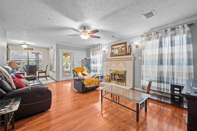 living room with hardwood / wood-style flooring, ceiling fan, a fireplace, ornamental molding, and a textured ceiling