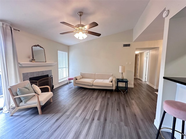 living room featuring vaulted ceiling, ceiling fan, a tiled fireplace, and wood-type flooring