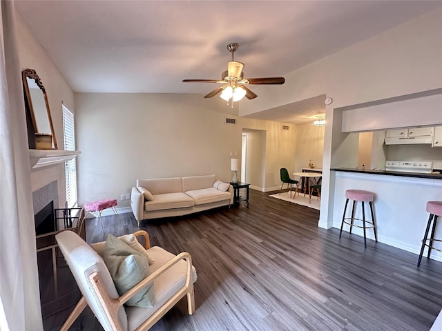 living room with ceiling fan, dark hardwood / wood-style flooring, a tiled fireplace, and vaulted ceiling