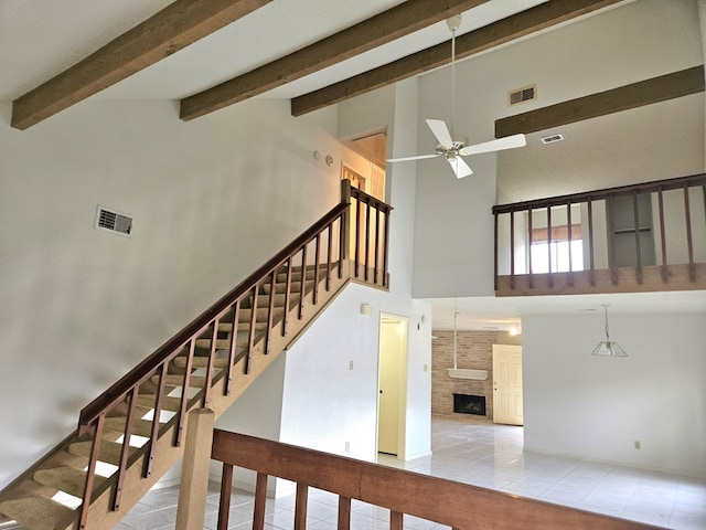 stairway with ceiling fan, tile patterned flooring, a large fireplace, and a high ceiling