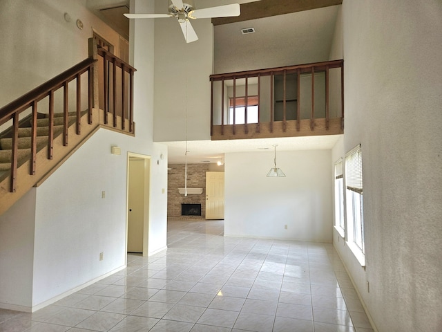 unfurnished living room with ceiling fan, light tile patterned floors, a fireplace, and a high ceiling