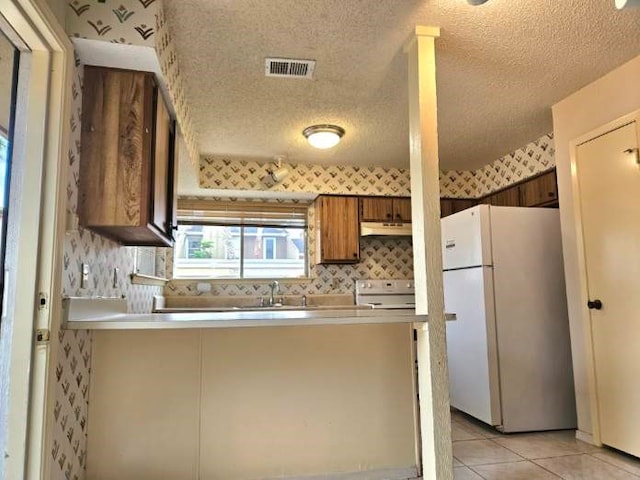 kitchen featuring sink, white appliances, light tile patterned floors, and a textured ceiling