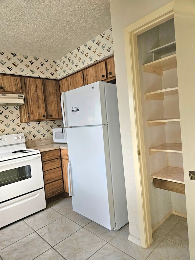 kitchen with a textured ceiling, light tile patterned flooring, and white appliances