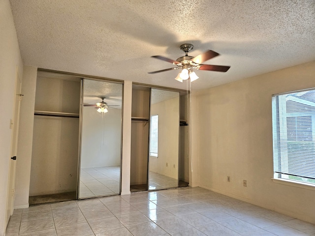 unfurnished bedroom featuring ceiling fan, light tile patterned floors, multiple closets, and multiple windows