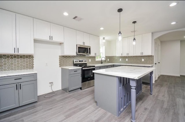 kitchen featuring a kitchen island, white cabinetry, stainless steel appliances, hanging light fixtures, and gray cabinetry