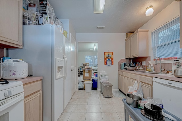 kitchen with sink, white appliances, a textured ceiling, light tile patterned floors, and light brown cabinetry