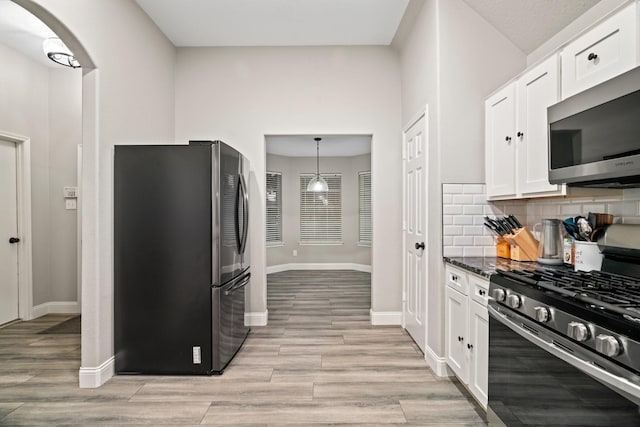 kitchen with pendant lighting, white cabinetry, backsplash, stainless steel appliances, and light hardwood / wood-style flooring