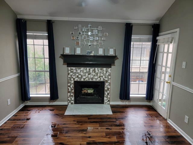 unfurnished living room with dark wood-type flooring, lofted ceiling, crown molding, and a tile fireplace