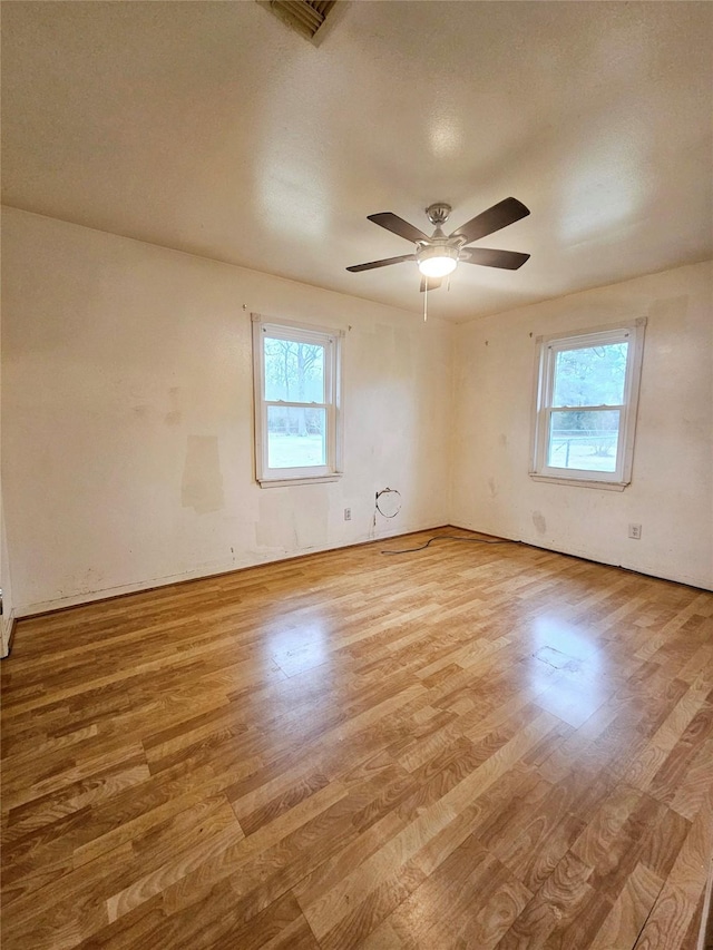 empty room featuring ceiling fan, a healthy amount of sunlight, and light hardwood / wood-style flooring