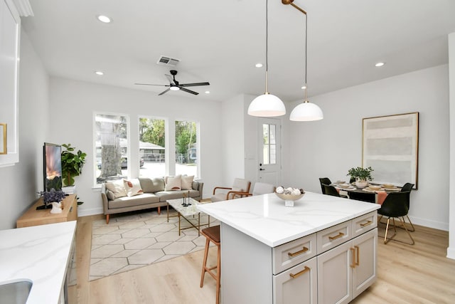 kitchen with decorative light fixtures, light wood-type flooring, light stone countertops, a breakfast bar, and a center island