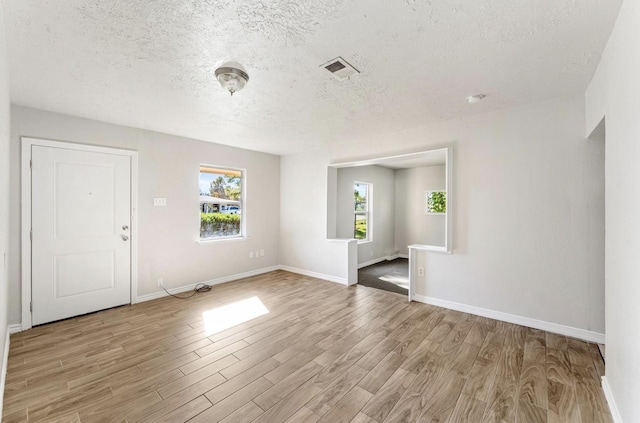 unfurnished room with a textured ceiling, a wealth of natural light, and light hardwood / wood-style flooring