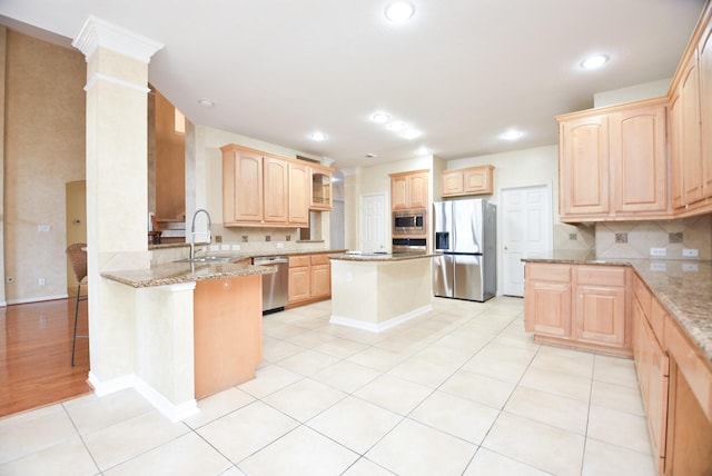 kitchen with kitchen peninsula, stainless steel appliances, light brown cabinets, light stone counters, and sink