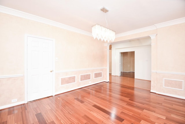 spare room featuring decorative columns, wood-type flooring, crown molding, and an inviting chandelier